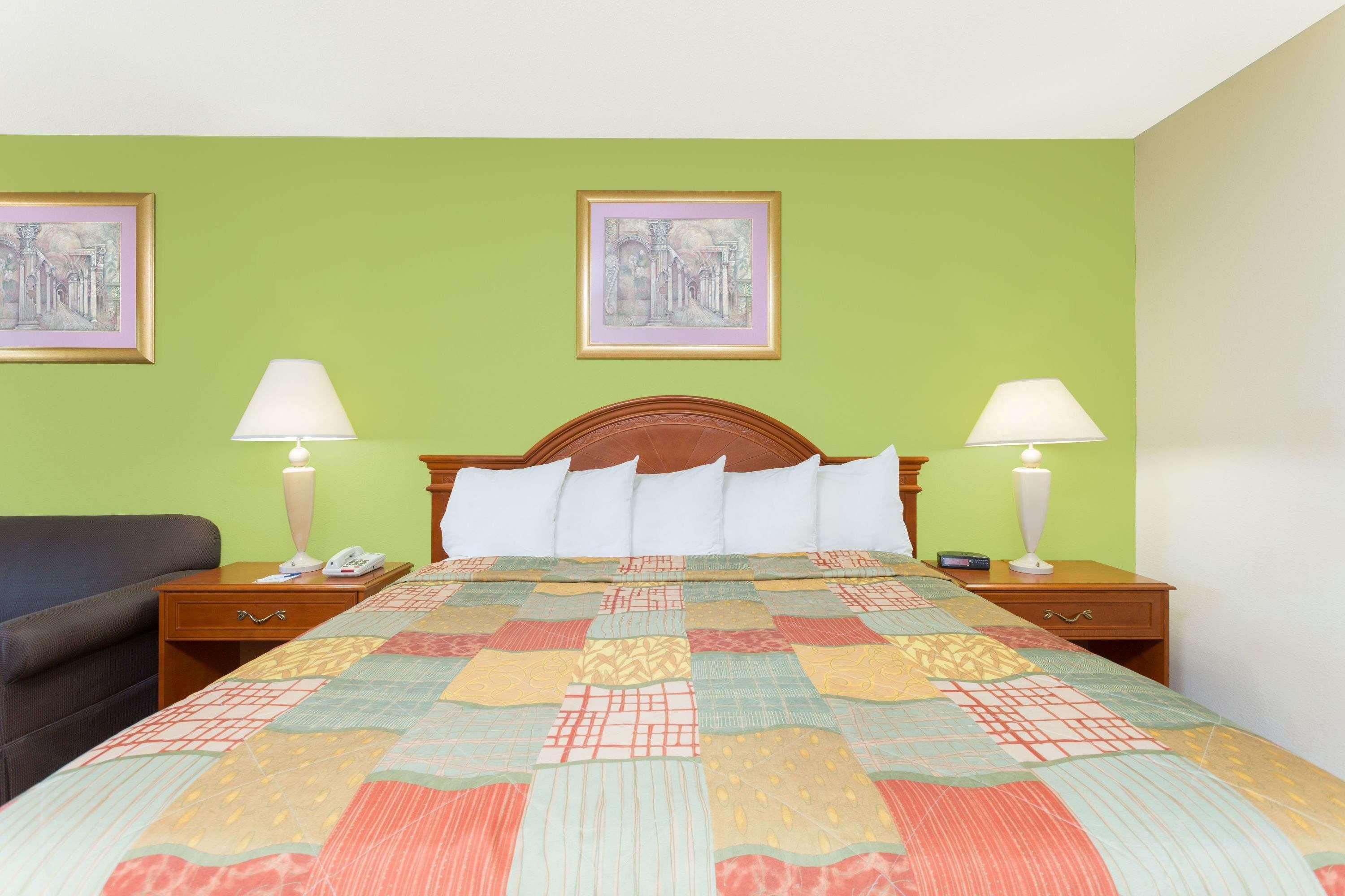 A hotel room with a bed, two bedside tables, a nightstand, a lamp, a chair, and two framed pictures on the wall.