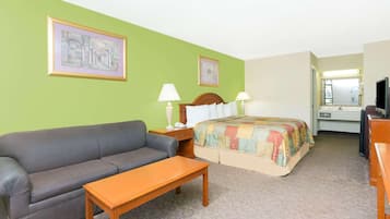 A hotel room with a sofa, a bed with a colorful quilt, two bedside tables with lamps, a wooden nightstand, and a television.