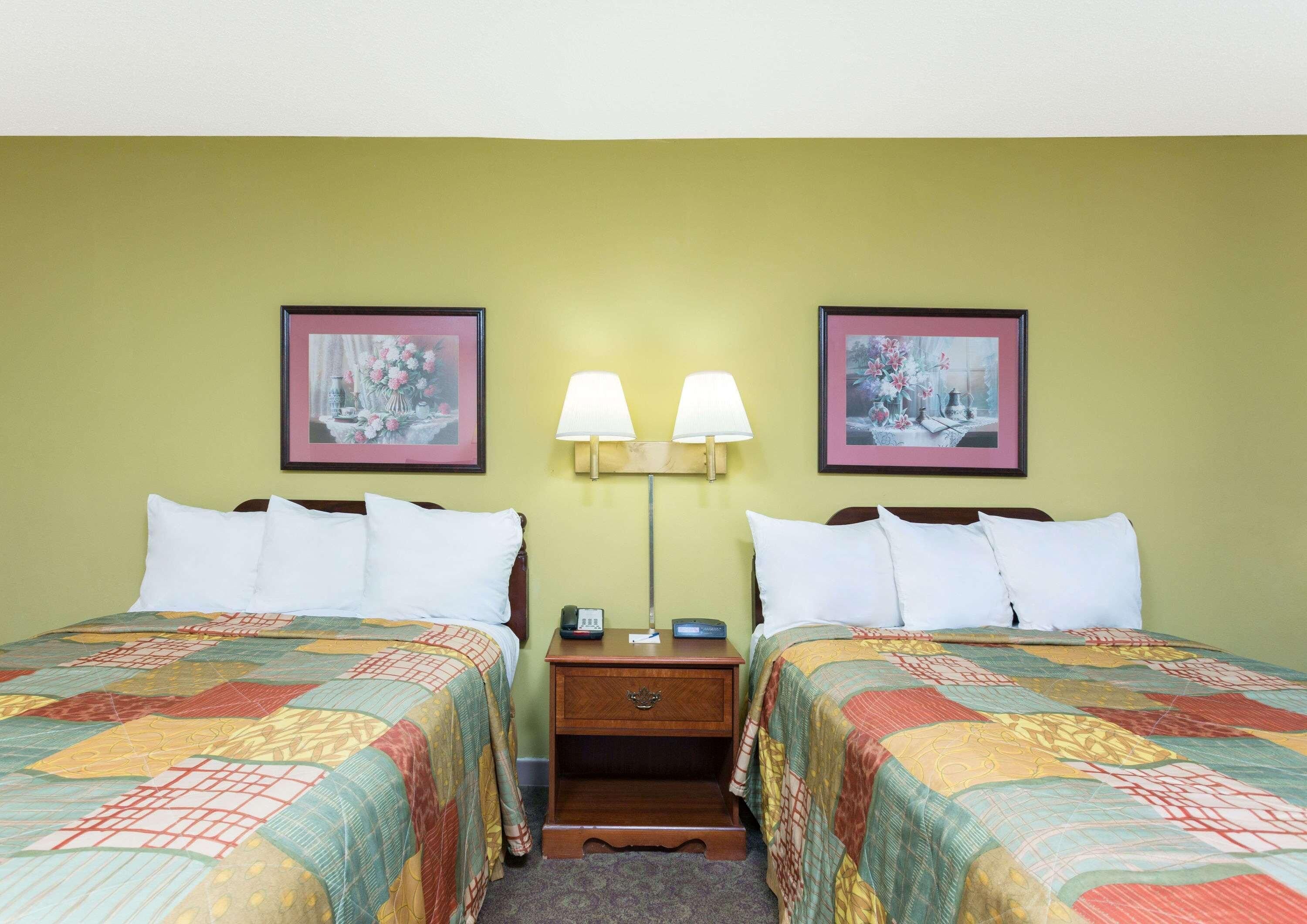 A hotel room with two beds, each with a quilted bedspread, a nightstand with a lamp, and two framed pictures on the wall.