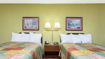 A hotel room with two beds, each with a quilted bedspread, a nightstand with a lamp, and two framed pictures on the wall.