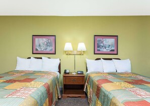 A hotel room with two beds, each with a quilted bedspread, a nightstand with a lamp, and two framed pictures on the wall. - Days Inn by Wyndham Clemson (Clemson)