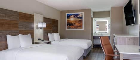 A hotel room with two beds, a desk, a chair, a TV, a painting, and a bathroom mirror.