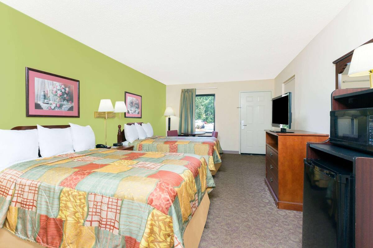A hotel room with two beds, a television, a desk, and a window with a view.