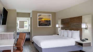 A hotel room with a bed, a desk, a chair, a TV, a painting, and a nightstand with a phone.