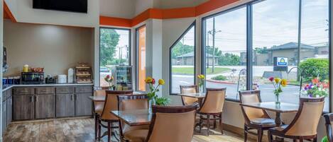 A restaurant with a kitchen area, large windows, and wooden flooring.