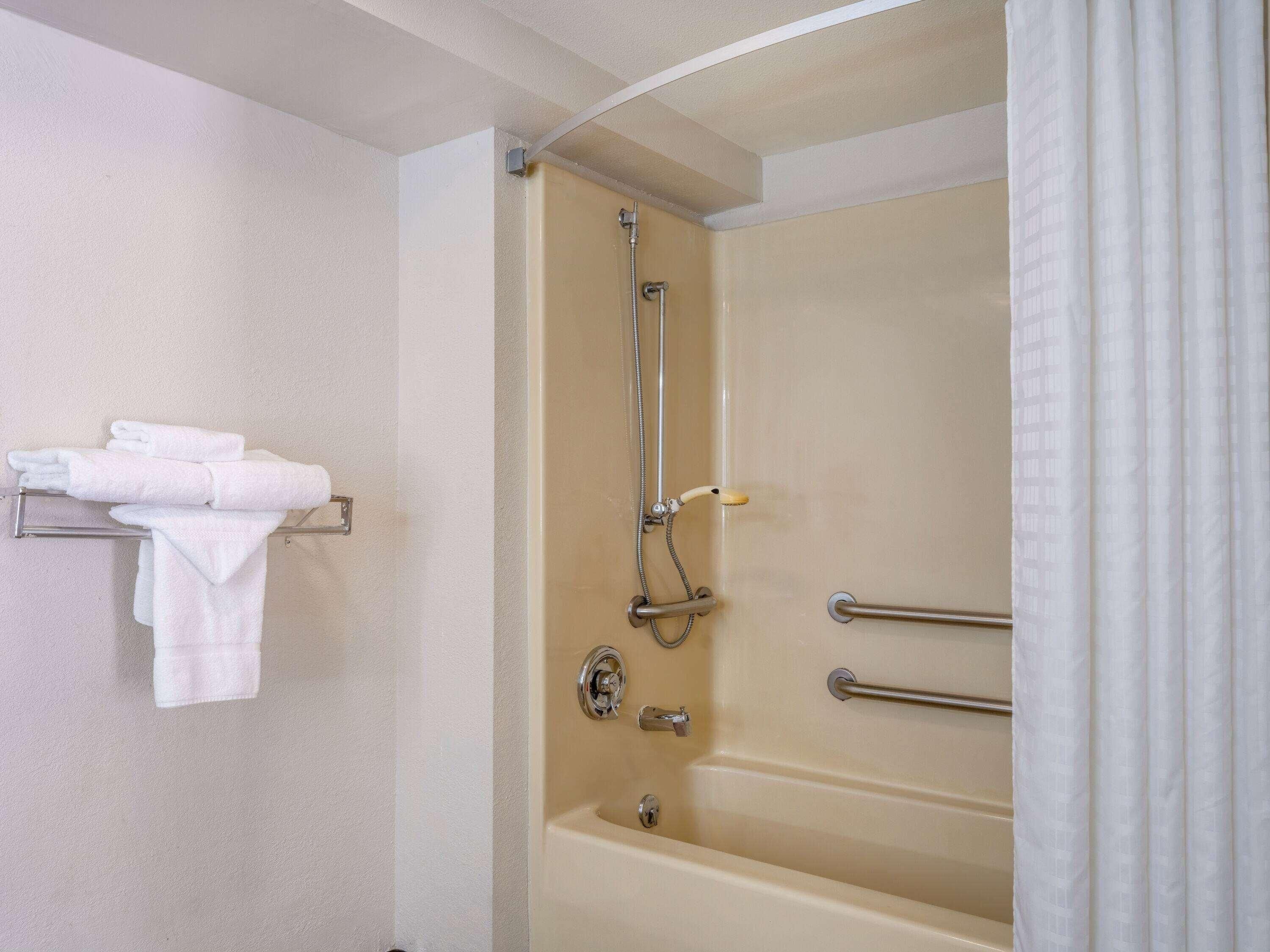 A bathroom with a bathtub, a towel rack with towels, and a shower curtain.