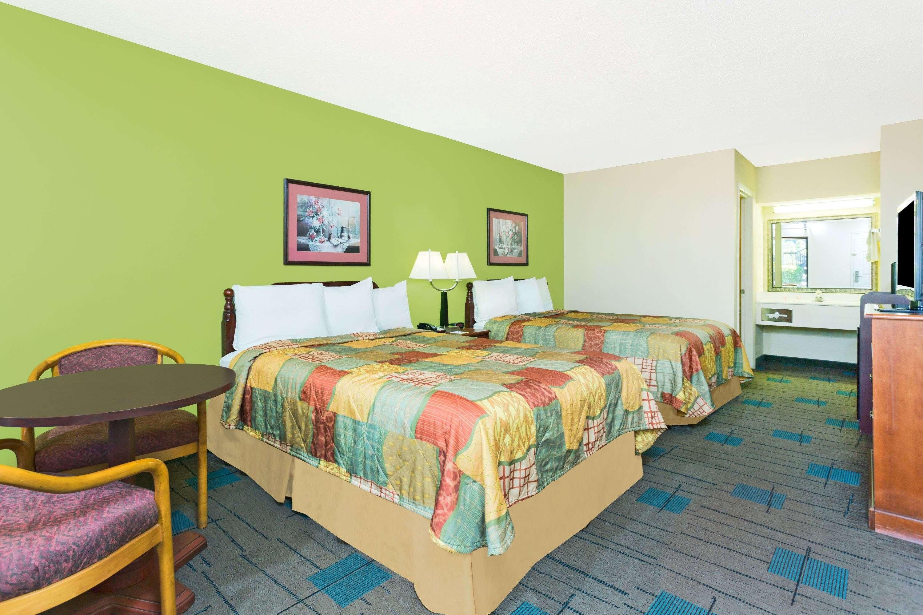 A hotel room with two beds, a desk, a chair, and a bathroom visible through an open door.