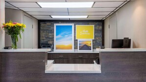 A reception desk with a vase of flowers, framed pictures, and a printer. - Days Inn by Wyndham Clemson (Clemson)