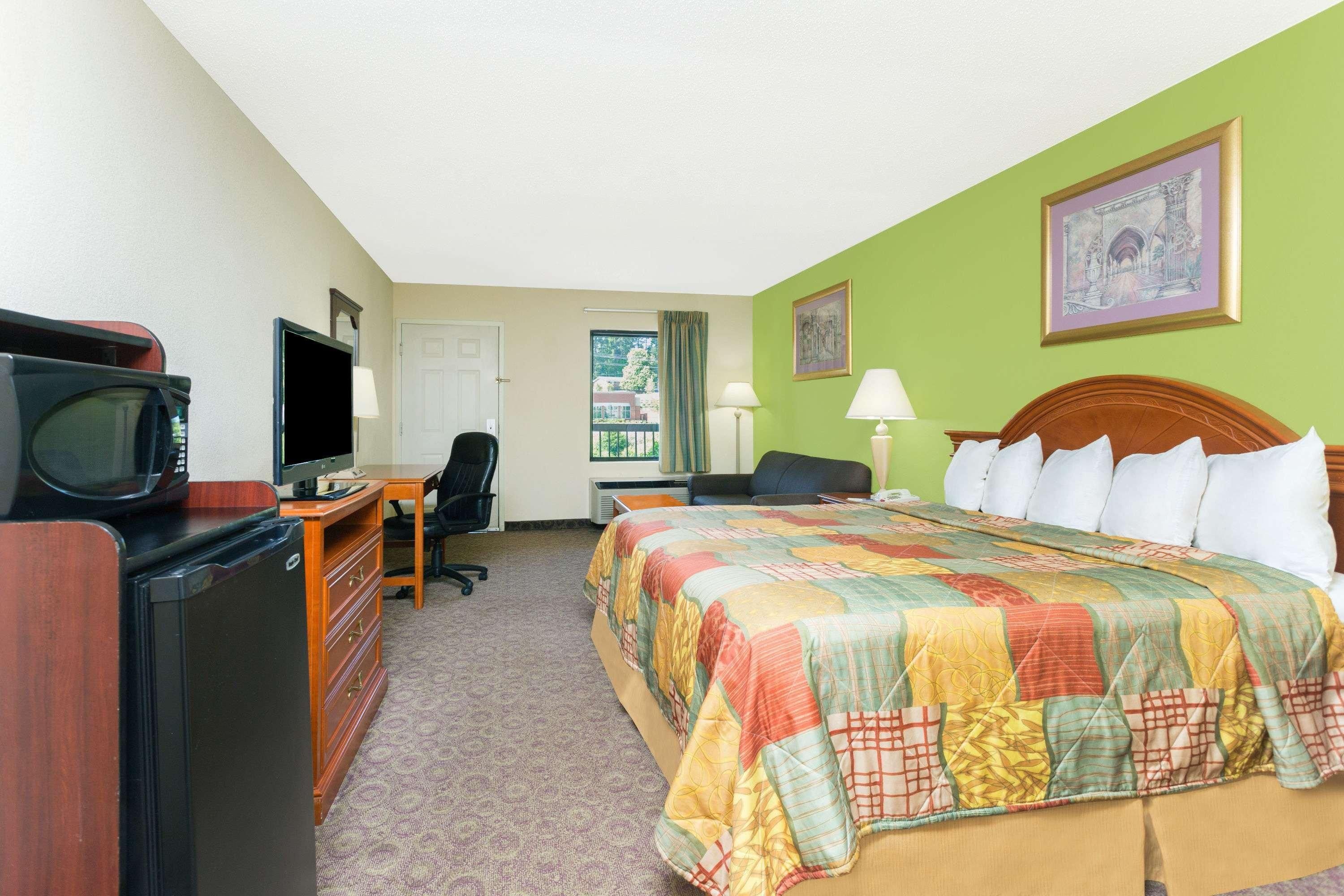 A hotel room with a bed, desk, television, and a window with curtains.
