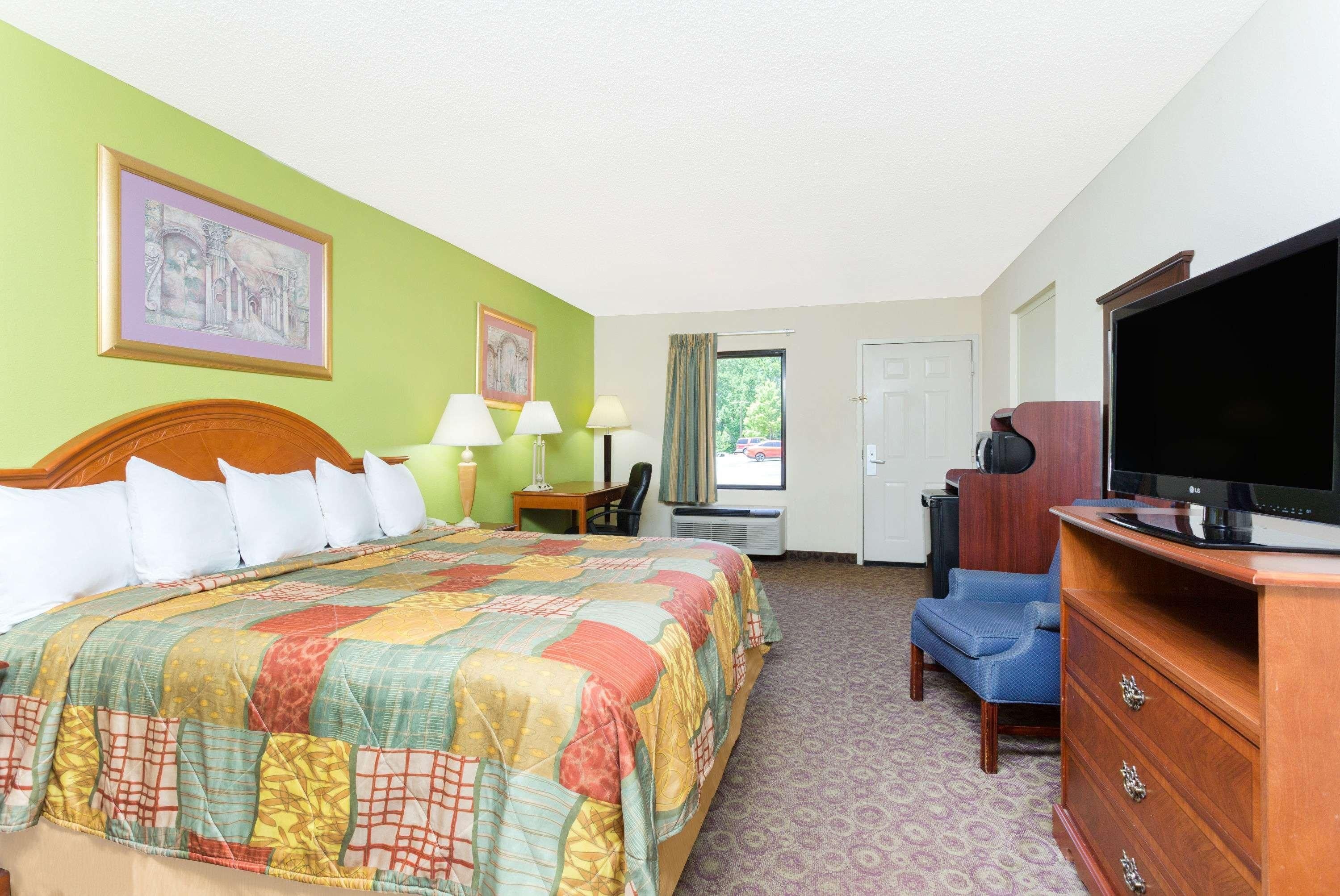 A hotel room with a large bed, a television, a desk with a chair, and a window with a view of the outside.