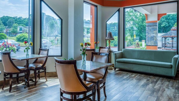 A dining area with a table and chairs, large windows, and a green sofa. - Days Inn by Wyndham Clemson (Clemson)