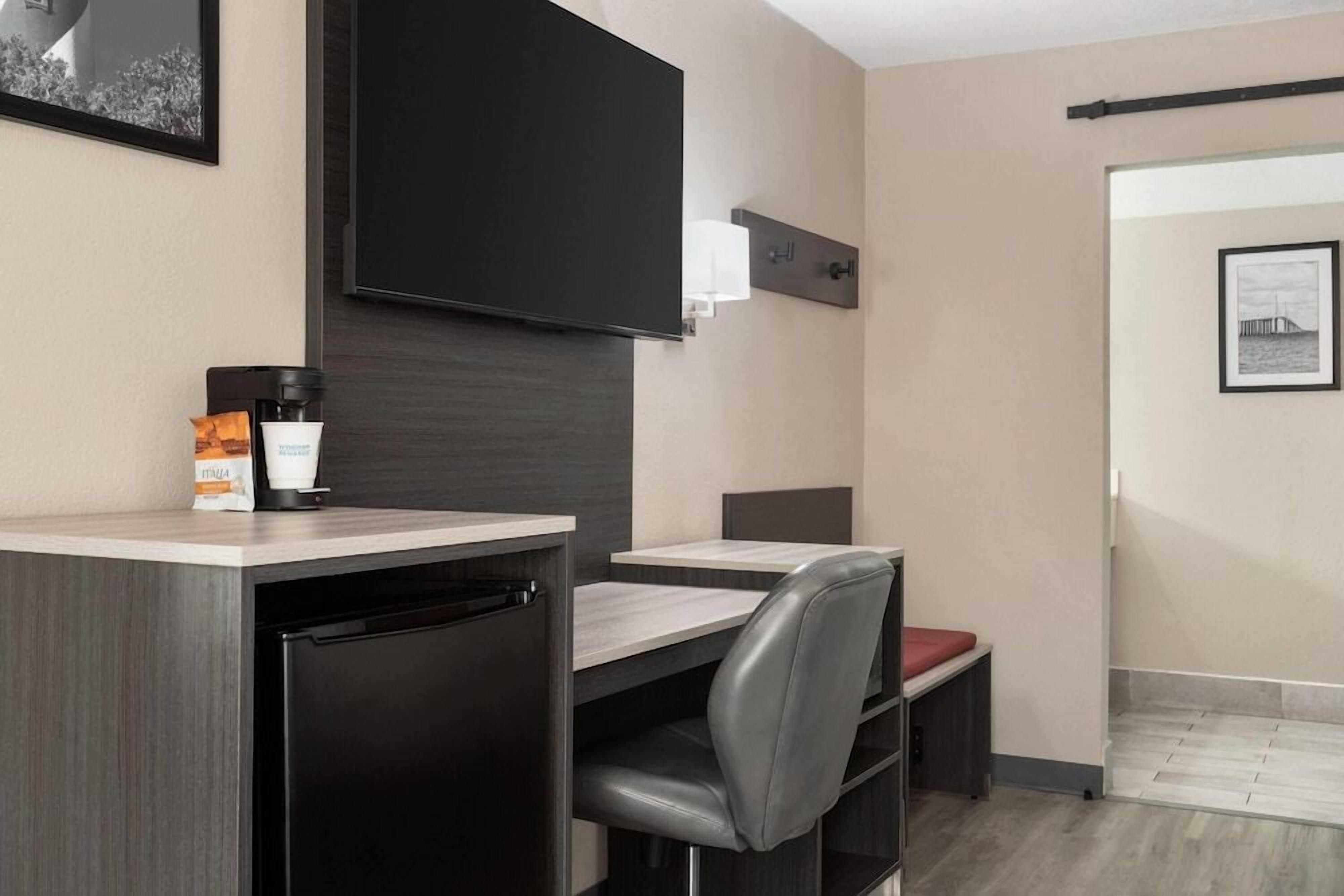 A hotel room with a kitchenette, a flat-screen TV, a small dining table, and a single chair.