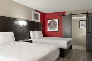 Habitación de hotel con dos camas, una pared de acento roja, un mapa mundial enmarcado y una puerta corrediza.