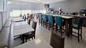 A modern dining area with a long counter, multiple seating options including booths and tables, and a kitchen area with appliances and a coffee machine. - Ramada by Wyndham Cocoa (Cocoa)