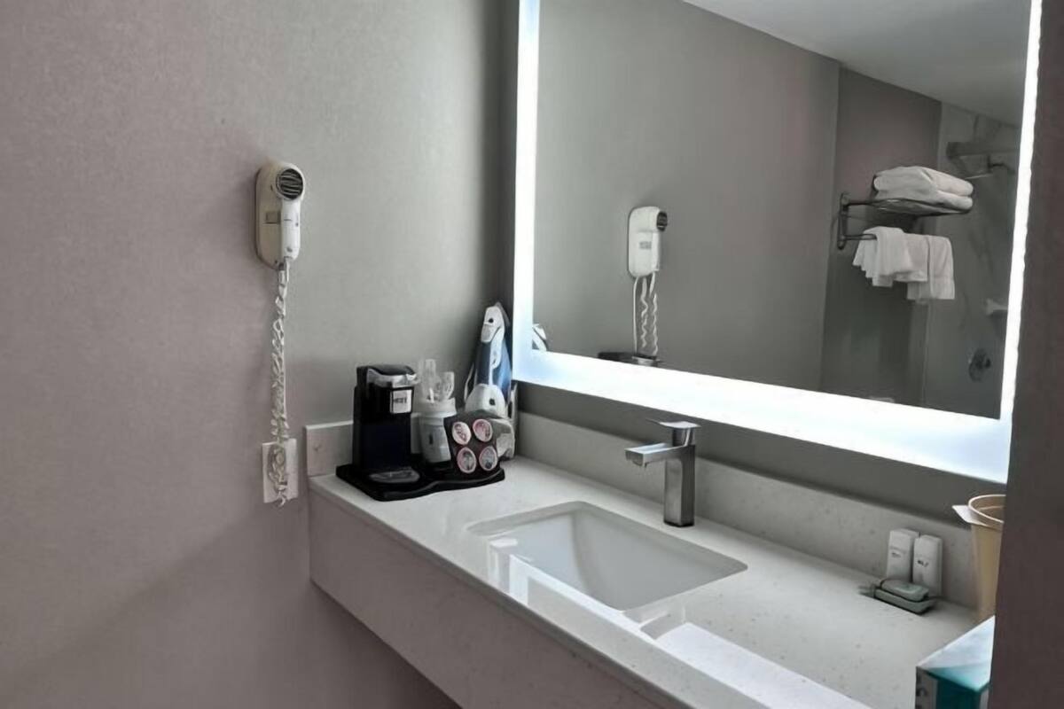 Une salle de bain d’hôtel équipée d’un lavabo, d’un miroir, d’un sèche-cheveux et d’un porte-serviettes.