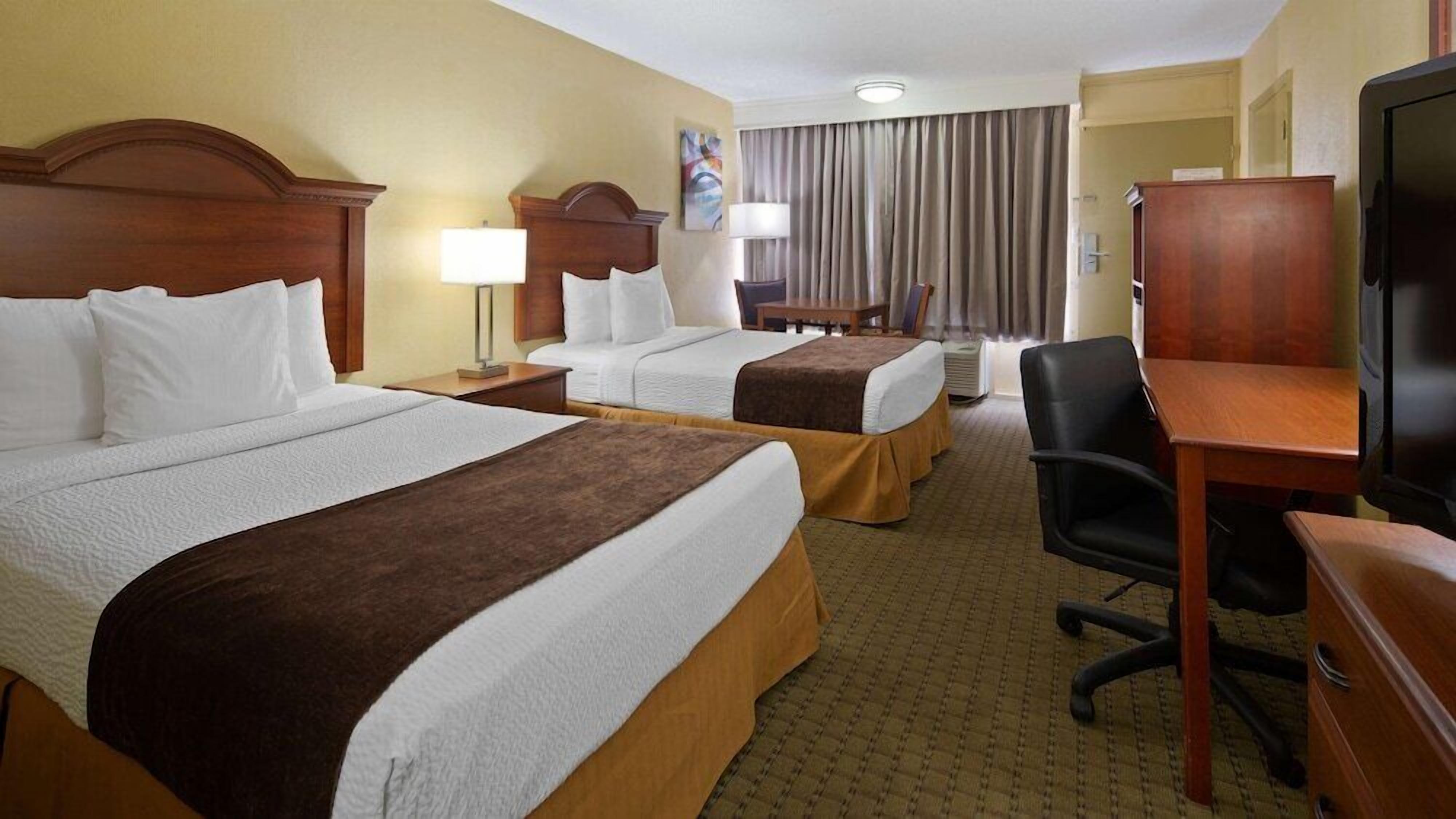 A hotel room with two beds, a desk, a chair, a television, and a window with curtains.