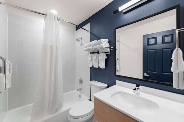 Ein modernes Badezimmer mit Duschkabine aus Glas, weißer Toilette, Waschbecken mit Spiegel und Handtuchhalter mit gefalteten Handtüchern.