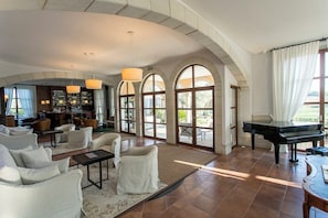 A spacious living room with a grand piano, comfortable seating, a bar area, and large arched windows. - Hotel Casa Anamaria (Vilademuls)