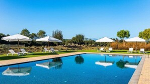 Una piscina amb gandules i ombrel·les, envoltada de vegetació i arbres.