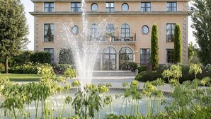 Un edifici gran de dos pisos amb una façana simètrica, una entrada central apuntada i una fontera al primer pla.