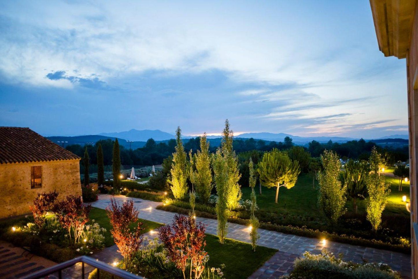 A landscaped garden with pathways, trees, and a building with a tiled roof.