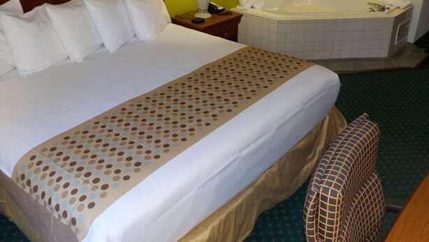Une chambre d’hôtel avec un grand lit, une baignoire séparée et une petite table avec une lampe.
