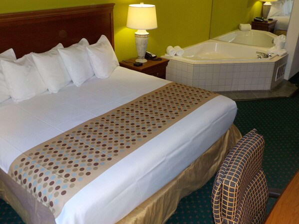 Une chambre d  ’hôtel avec un grand lit, une baignoire séparée et une petite table avec une lampe.