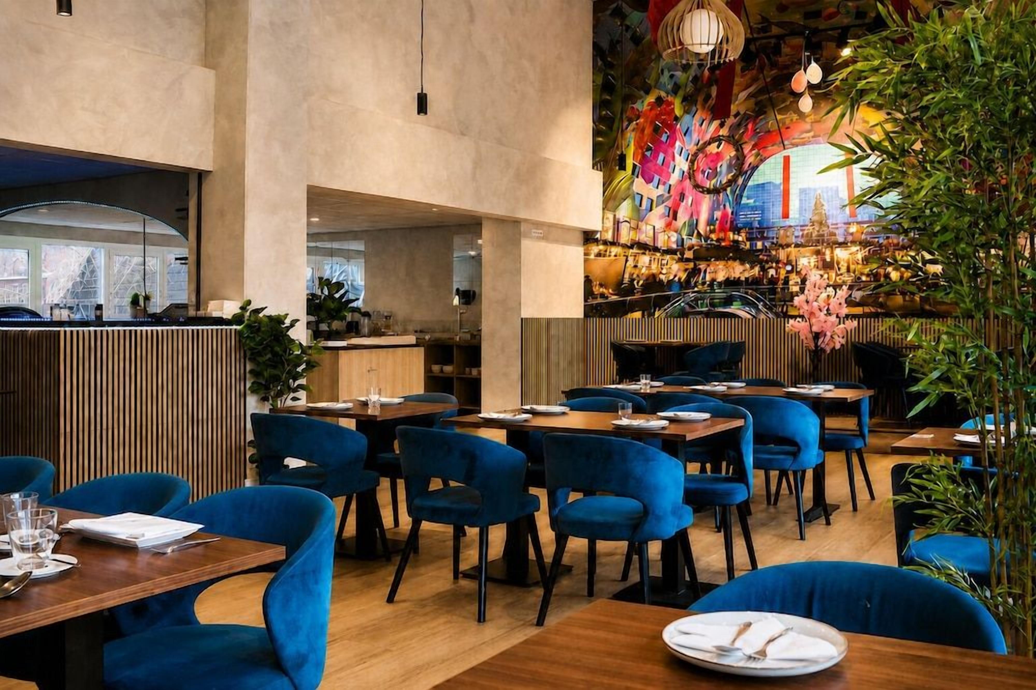 A restaurant with blue upholstered chairs, wooden tables, and a colorful mural on the wall.