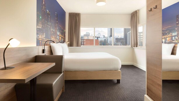 A hotel room with a bed, a desk, a chair, a window with a cityscape view, and a large poster on the wall. - Rotterdam Teleport Hotel (Rotterdam)