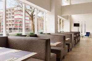 A modern restaurant with high tables and booths, large windows, and a flat-screen TV on the wall. - Rotterdam Teleport Hotel (Rotterdam)