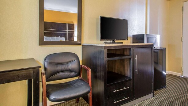 Een hotelkamer met een grote spiegel, een flatscreen televisie, een kleine koelkast, een bureau en een lederen fauteuil.