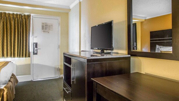 A hotel room with a bed, a desk, a television, a mirror, and a door with a window. - The Boards AC (Atlantic City)