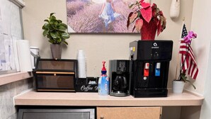 Een kleine keuken met een koffiezetapparaat, een kleine koelkast, een prullenbak en een potplant.