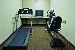 Una habitación con una cinta de correr, una bicicleta estática y un televisor sobre un escritorio.