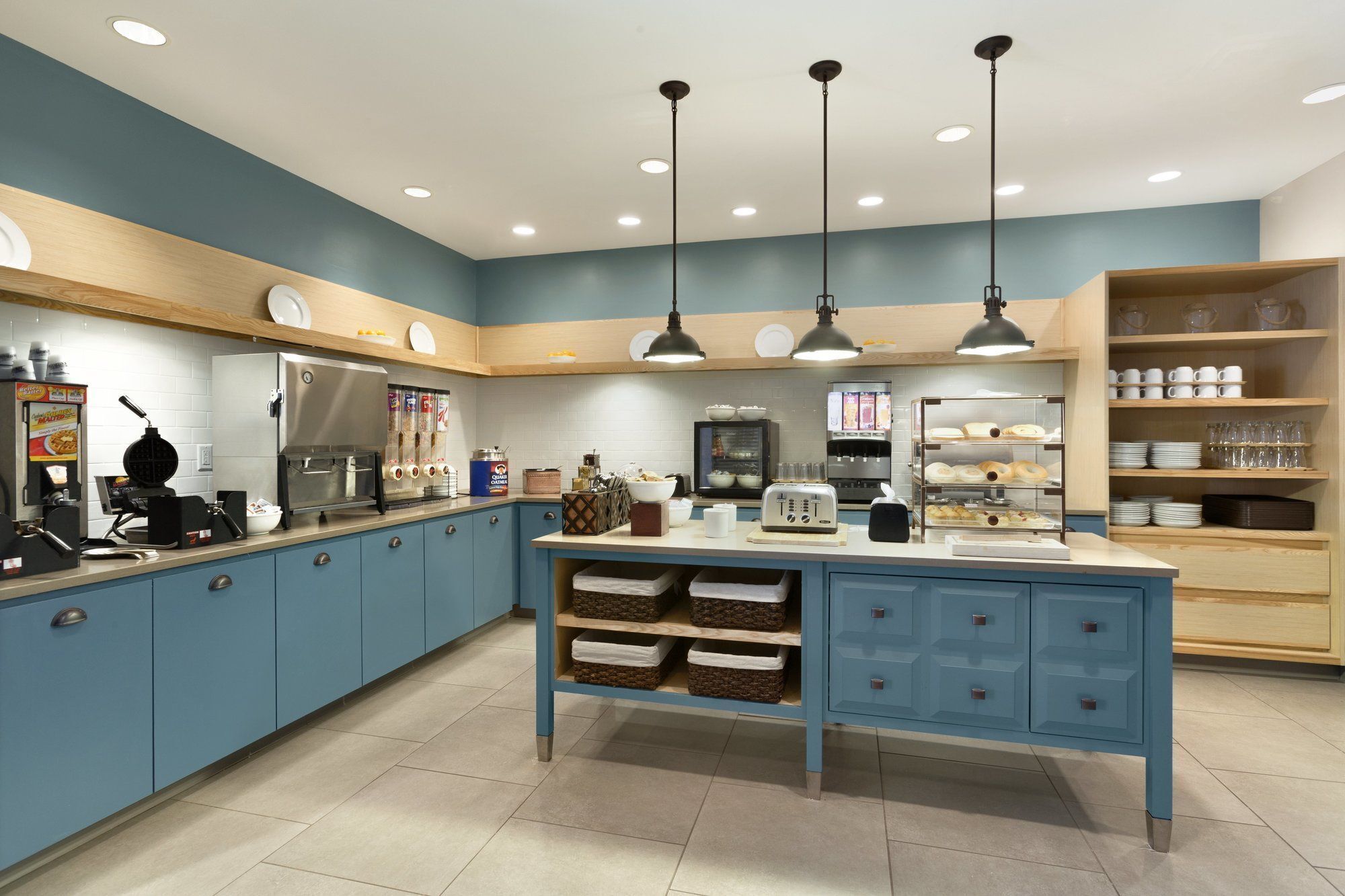 A kitchen with blue cabinets, a central island with drawers, overhead pendant lights, a coffee machine, a toaster, and a refrigerator.