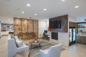 A modern living room with a sofa, armchairs, a coffee table, and a fireplace. There is a kitchen area with a refrigerator and a microwave. - Holiday Inn Express & Suites Marquette, an IHG Hotel (Marquette)