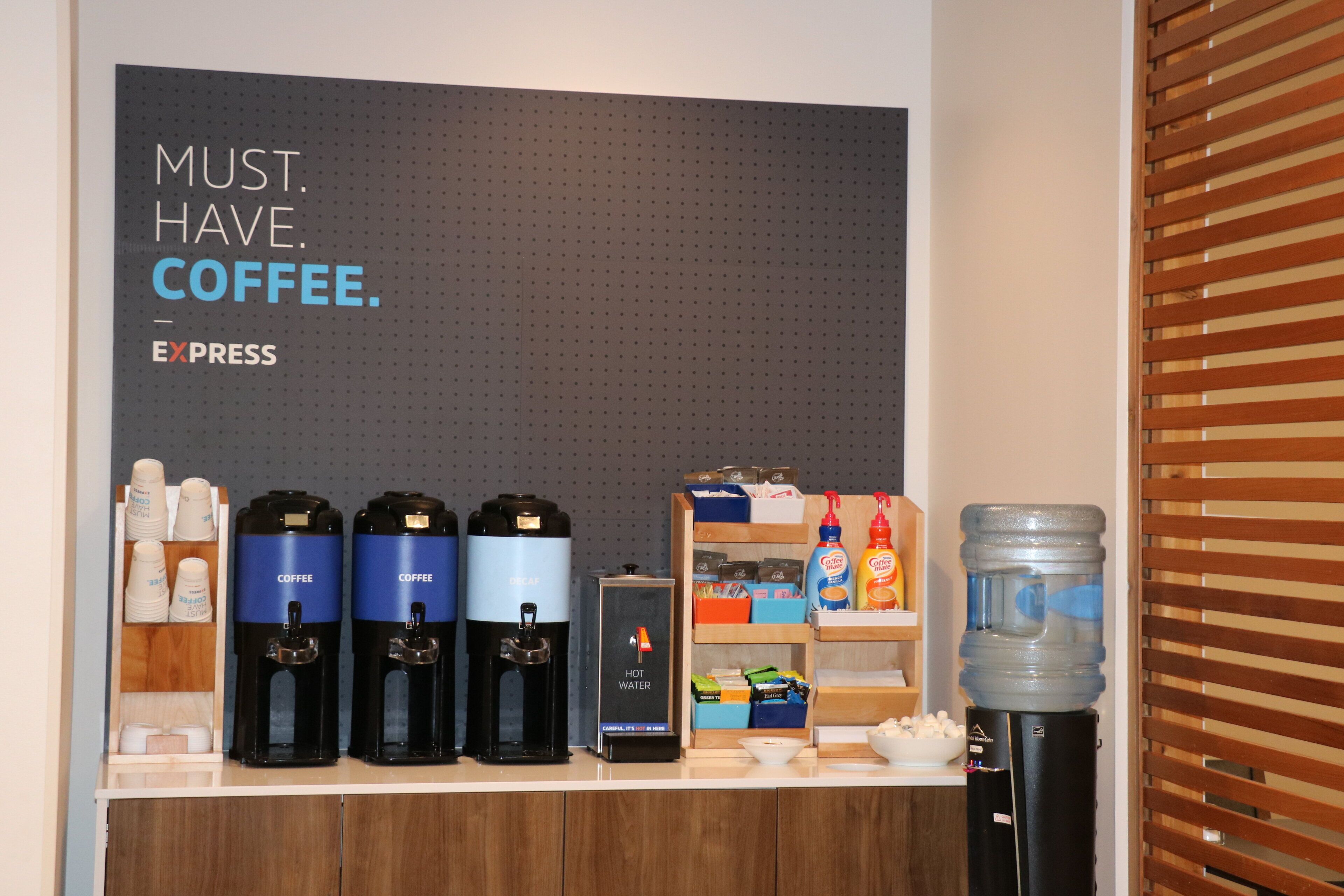 A coffee station with multiple coffee dispensers, a water cooler, and a shelf with snacks and condiments.