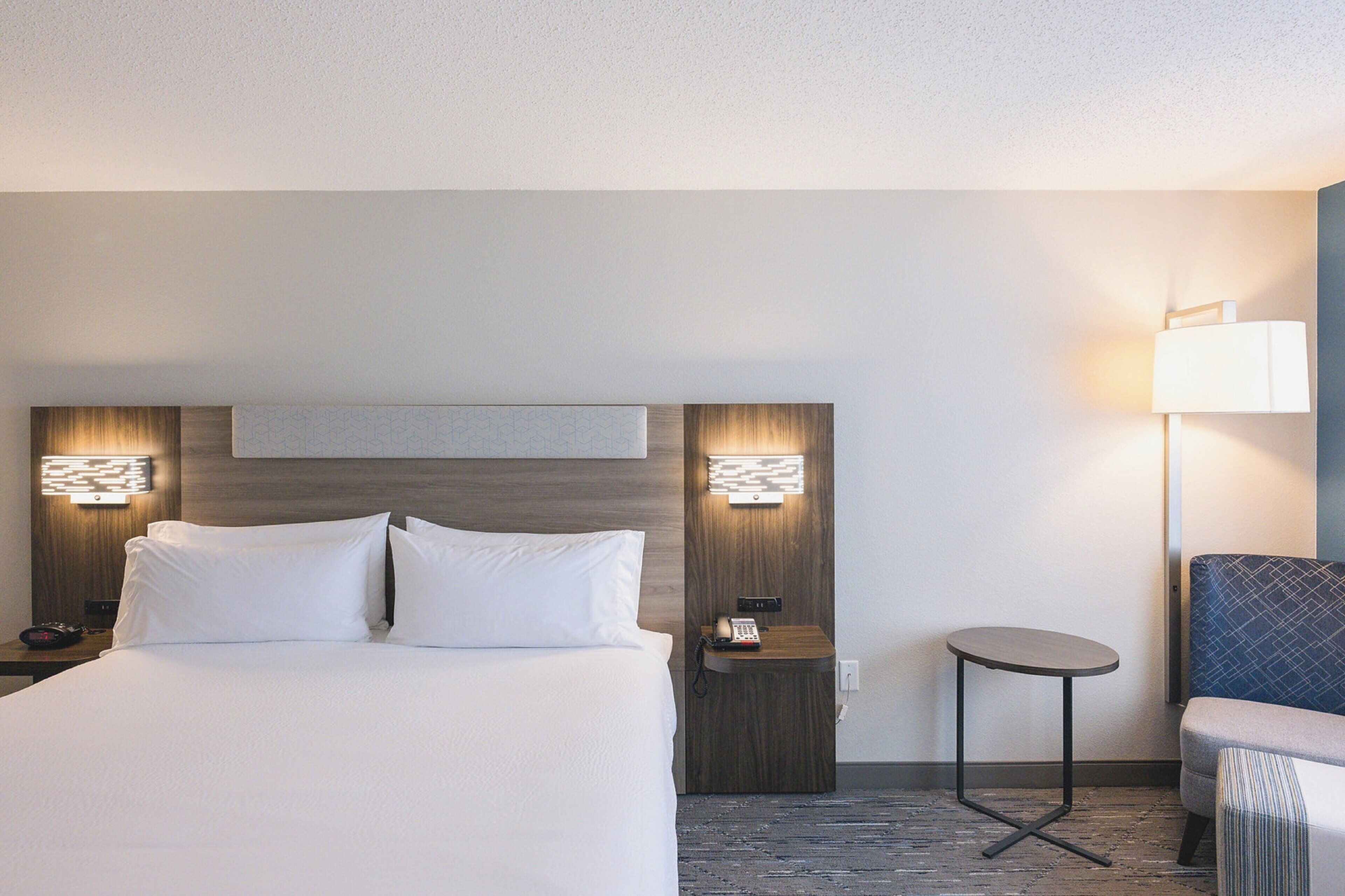 Ein Hotelzimmer mit einem großen Bett, Nachttischen mit Lampen, einem kleinen runden Tisch und einem Sessel.
