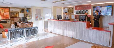 A hotel reception area with a modern design, featuring a reception desk, a seating area with a coffee table, and a large painting on the wall.