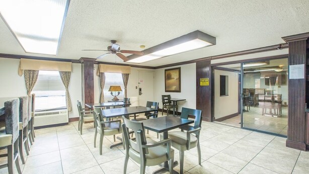 Un espace repas avec des tables et des chaises, un ventilateur de plafond et une vue sur une autre pièce, accessible par une porte vitrée.