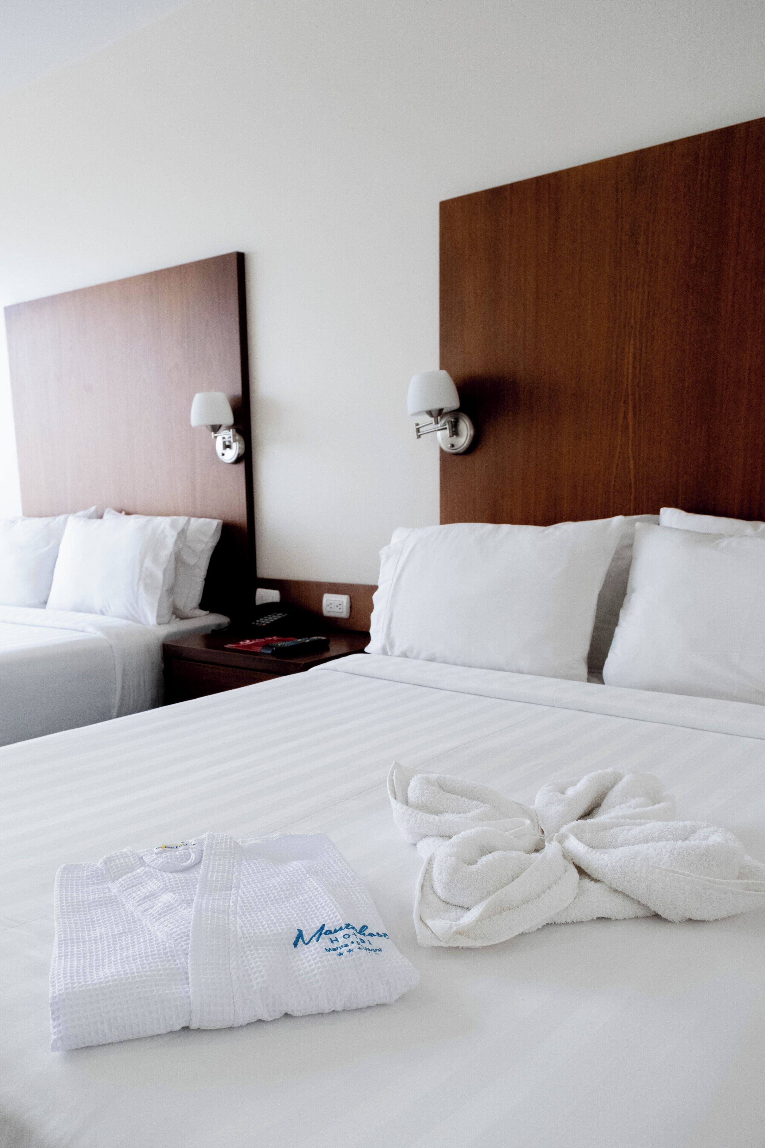 Una habitación de hotel con una cama grande, dos mesitas de noche, un cabecero de madera y una lámpara de pared.