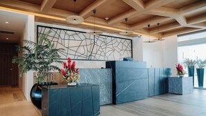 Un espace d’accueil au design moderne, comprenant un comptoir de réception en marbre, une grande œuvre d’art abstraite murale et des plantes en pot.