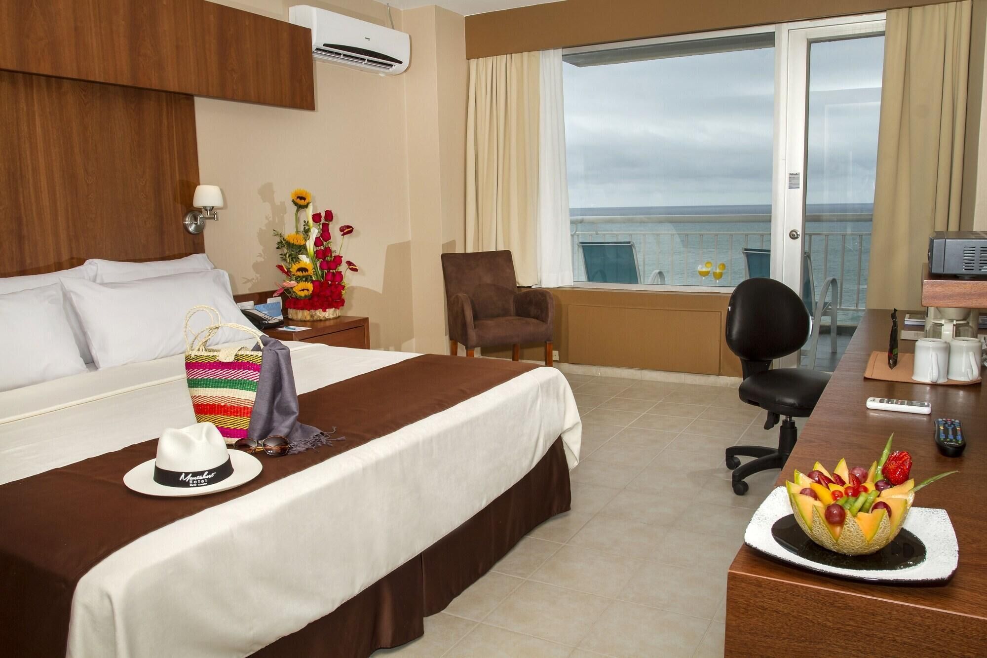 Habitación de hotel con cama, escritorio con computadora, silla y vista al mar.