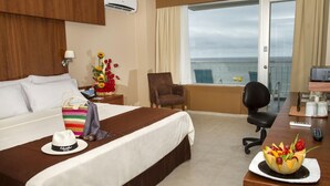 Une chambre d’hôtel avec un lit, un bureau équipé d’un ordinateur, une chaise et une vue sur la mer.