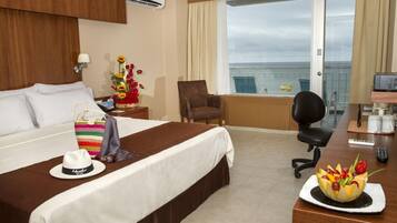 Habitación de hotel con cama, escritorio con computadora, silla y vista al mar.
