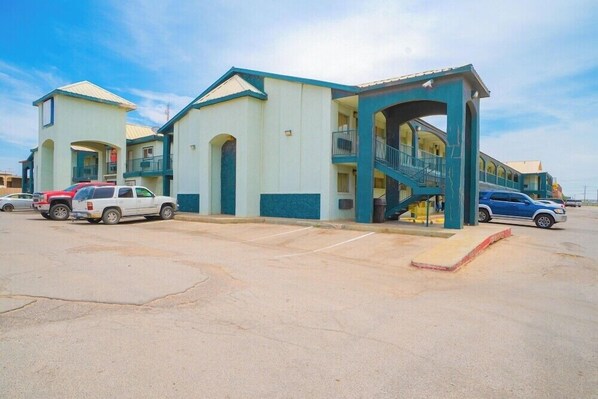 Un motel composé d’un bâtiment central et de deux ailes latérales, doté d’un espace de stationnement couvert et où plusieurs véhicules sont garés.