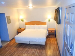 Une chambre d’hôtel avec un plancher en bois, un grand lit avec une literie blanche, deux tables de chevet avec des lampes et une porte fermée à clé.