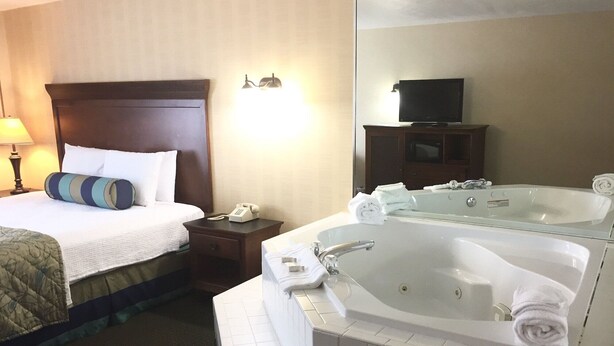 Ein Hotelzimmer mit Bett, Nachttisch, Telefon, großem Spiegel, Fernseher und einer Badewanne mit Handtüchern.