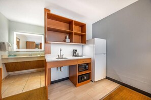 A compact kitchen with a built-in microwave, a refrigerator, and a wooden shelf unit.