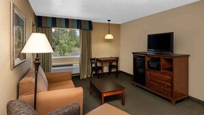 Ein Hotelzimmer mit einer Couch, einem kleinen Tisch, einem Fernseher auf einer Holzkommode und einem Fenster mit Vorhängen.